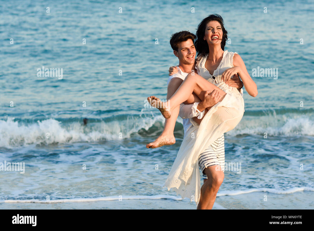 Feliz pareja joven caminando en una playa hermosa. Gracioso el hombre lleva  una mujer en sus brazos. Personas vestidas con ropa casual Fotografía de  stock - Alamy