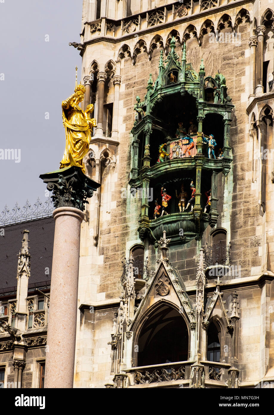 El Glockenspiel en la torre del reloj del ayuntamiento, Rathaus, Munich y en primer plano, en el centro de la Marienplatz, la columna Mariensäule Foto de stock