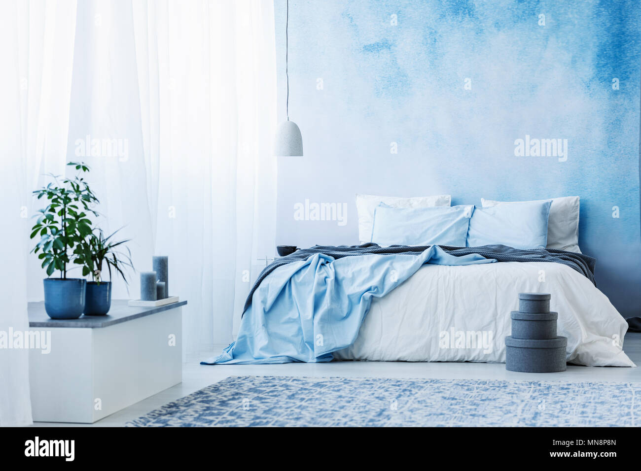 Azul cielo interior del dormitorio con cama doble, plantas y cuadros grises en el suelo Foto de stock