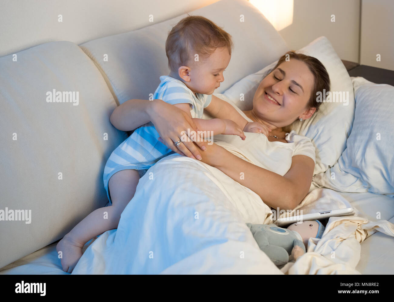 Retrato de cute Baby Boy acostado con la madre en la cama en la noche Foto de stock