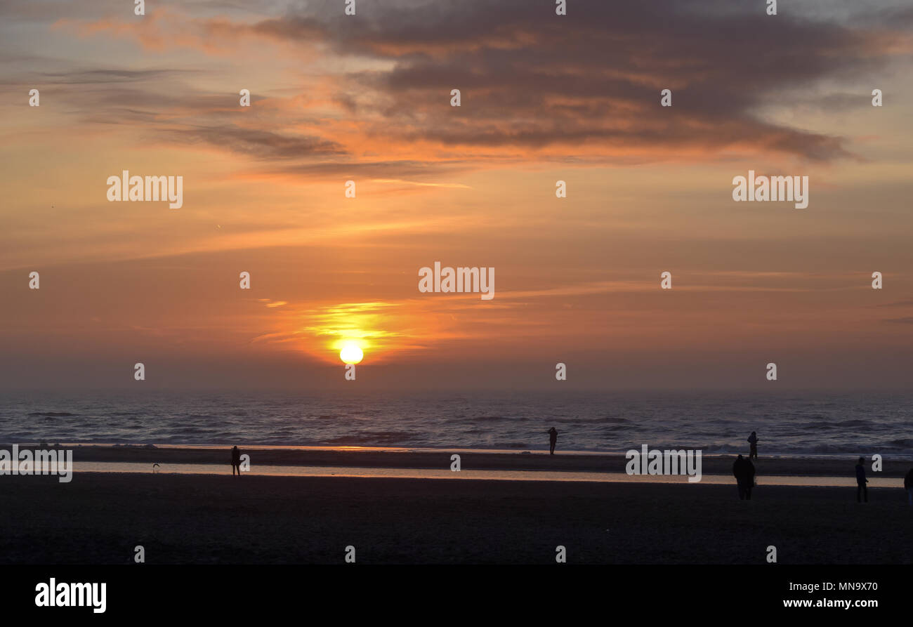 Puesta de sol con un cielo anaranjado en la playa con gente mirando en el boulevard. Foto de stock