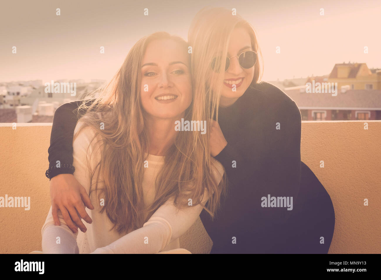 Sonrisa y diversión para una rubia chicas pareja en la terraza al aire libre. Los rayos de sol roodtop retroiluminación brillante imagen con amistad concepto. hermosas modelos h Foto de stock