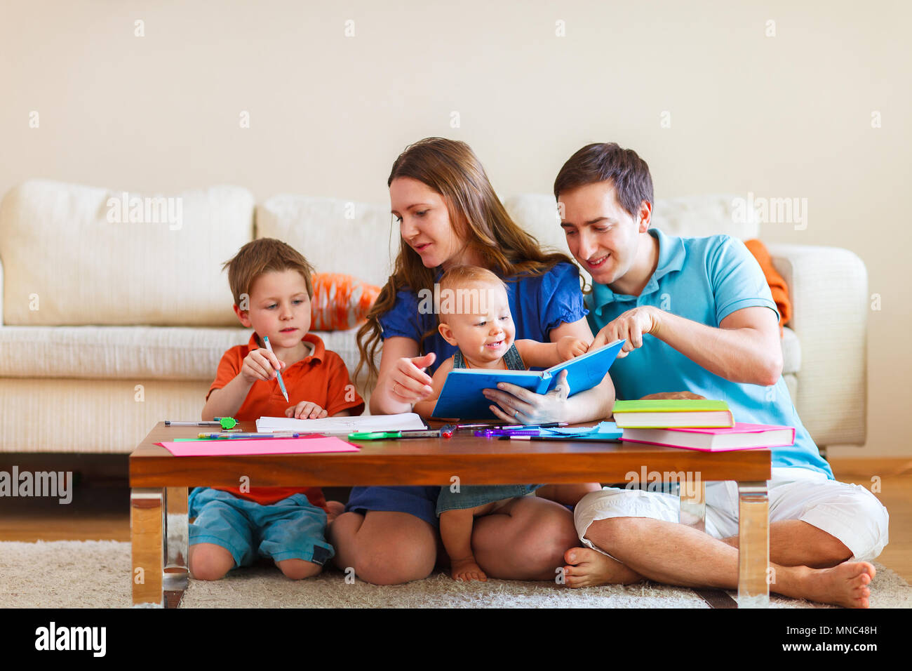 Una familia joven con dos niños de dibujo y leer juntos Foto de stock