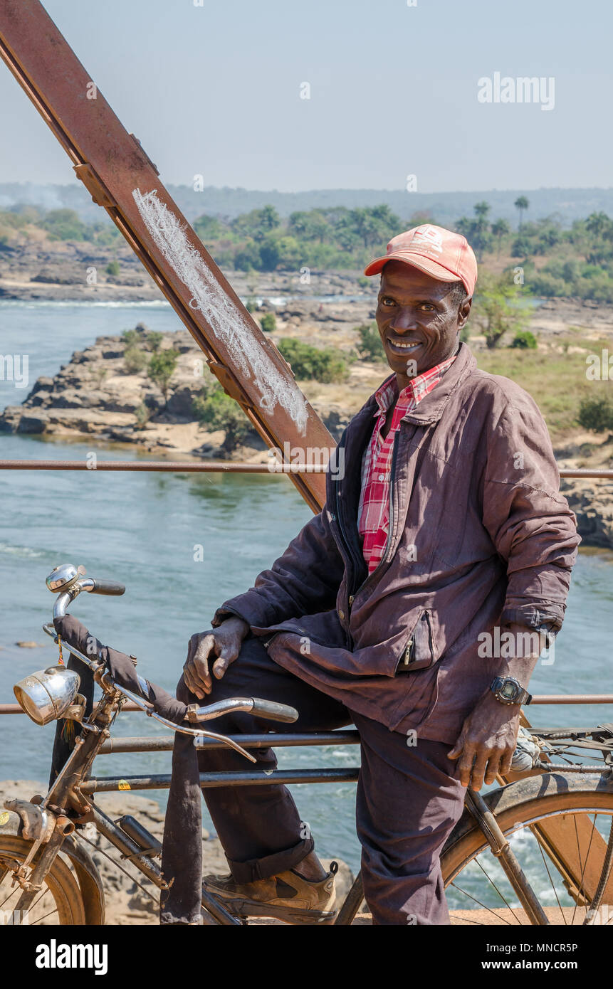 No Identificado hombre africano de mediana edad sentado sobre la bicicleta en el puente sobre el río Foto de stock