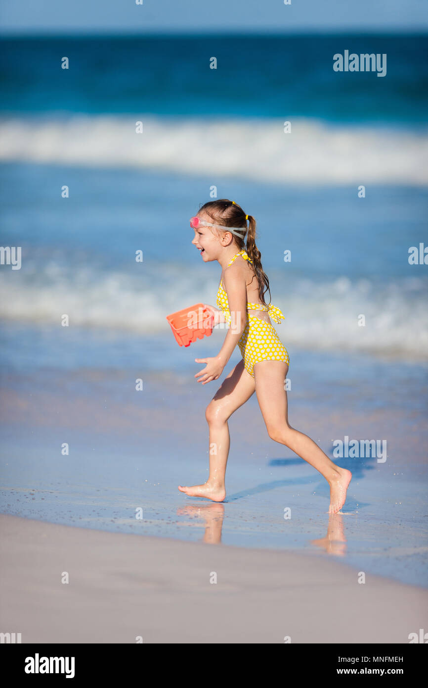 Feliz niña en un traje de baño amarillo corriendo en una playa con un  juguete de plástico, mientras que las vacaciones de verano Fotografía de  stock - Alamy