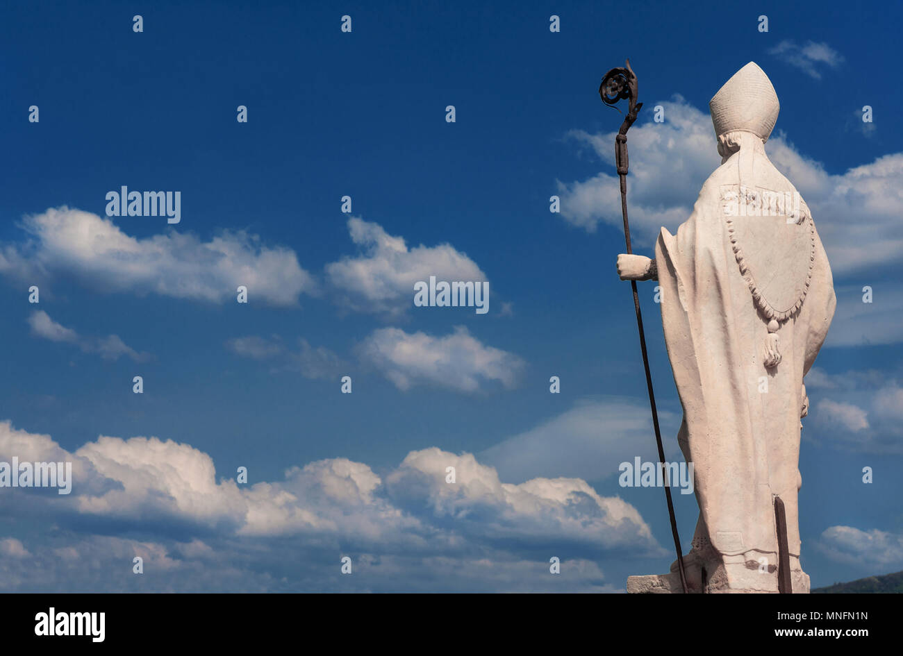 Obispo con crosier, cielo azul y nubes. Estatua de mármol blanco sobre las antiguas murallas de Lucca, erigida en el siglo XVII (con copia espacio) Foto de stock