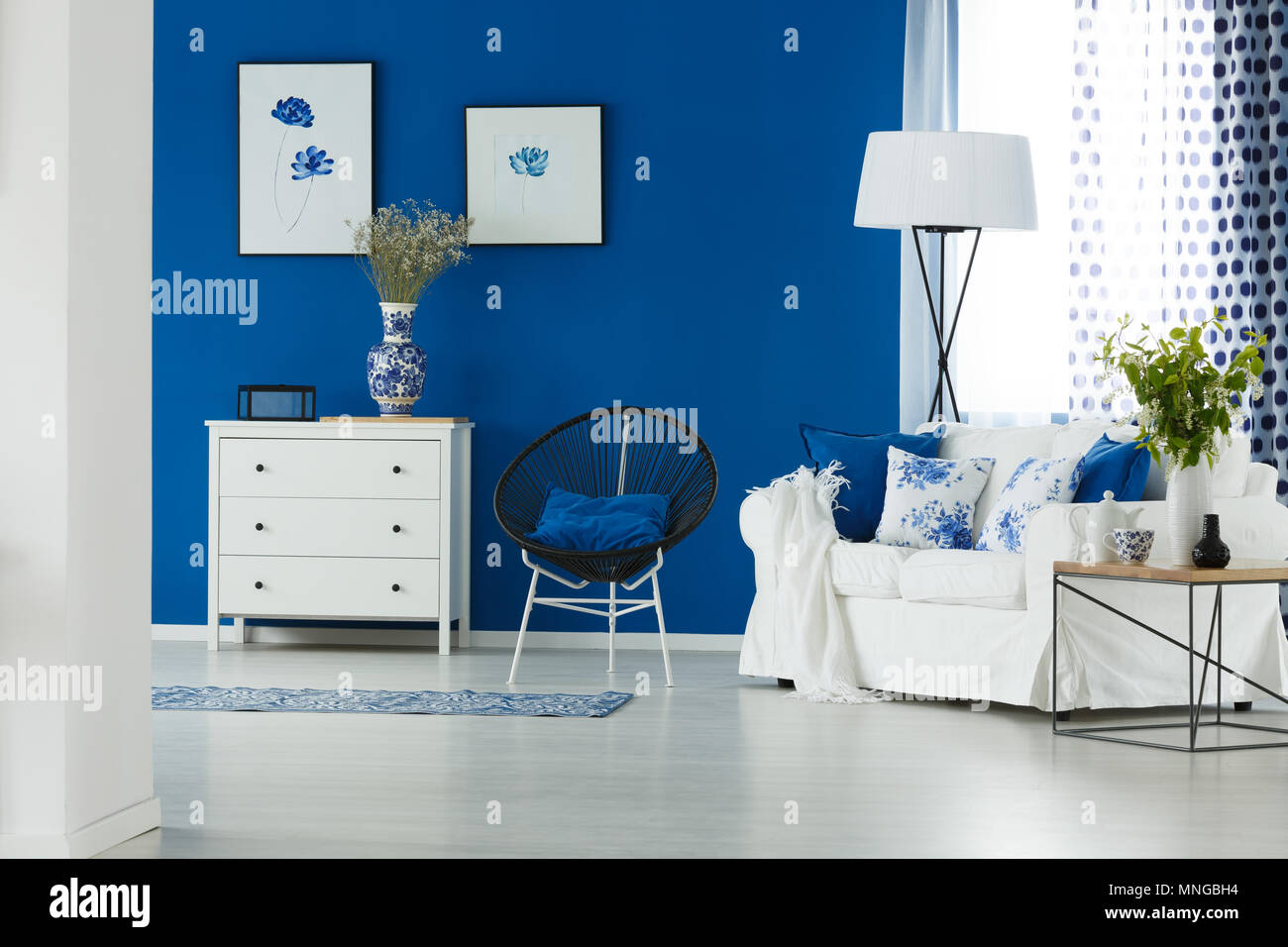 Sofá, silla, lámpara y cómoda en el salón azul y blanco Foto de stock