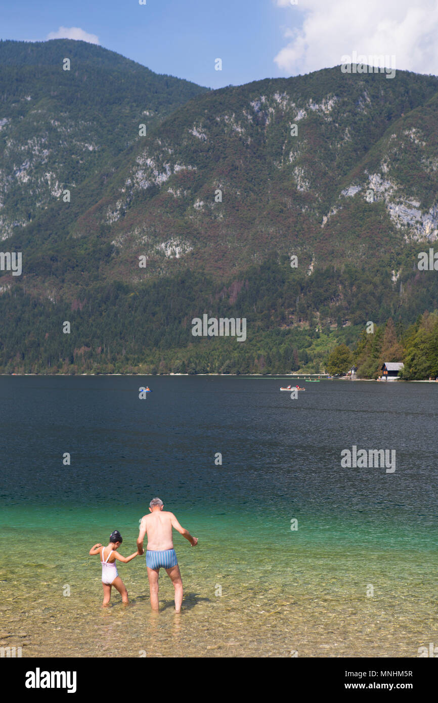 El abuelo sosteniendo la mano de su nieto al entrar en el agua fría del lago de Bohinj, el mayor lago permanente situado en el valle de Bohinj Alpes Julianos, el Parque Nacional de Triglav, en Eslovenia Foto de stock