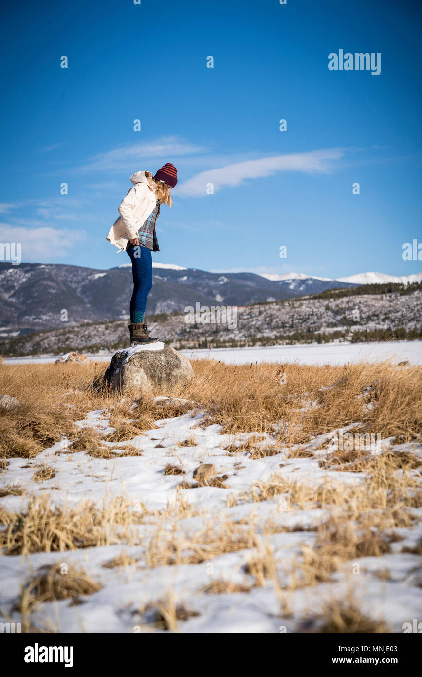Mujer joven de pie sobre una roca en los soleados días de invierno en Colorado, EE.UU. Foto de stock