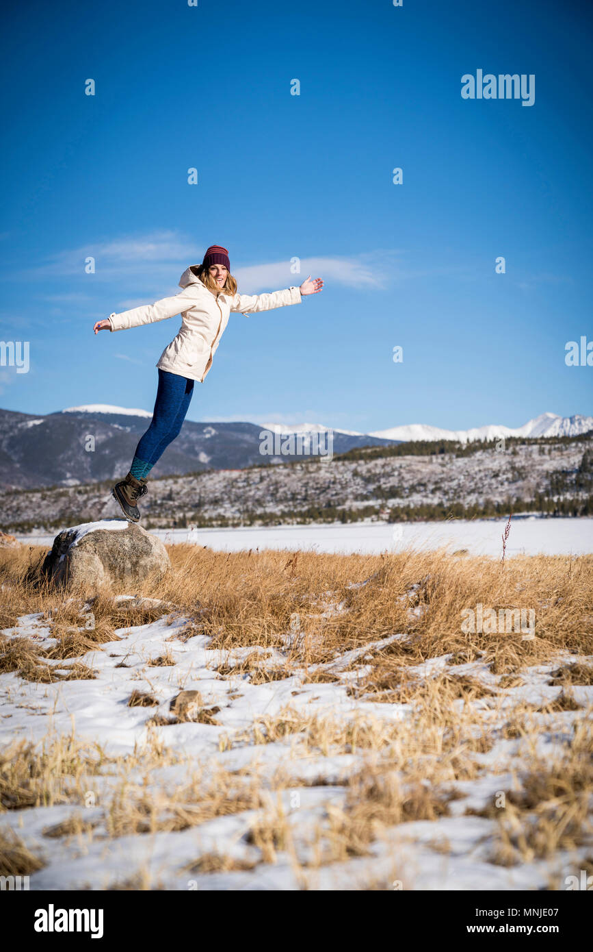 Mujer joven saltando en el aire exterior en los soleados días de invierno en Colorado, EE.UU. Foto de stock