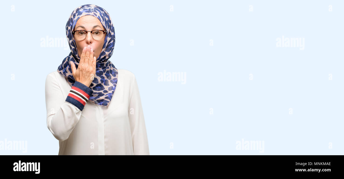 Edad media los árabes musulmanes mujer vistiendo el hijab cubre boca en estado de shock, parece tímido, expresando el silencio y confundir los conceptos, asustada aislados de fondo azul Foto de stock