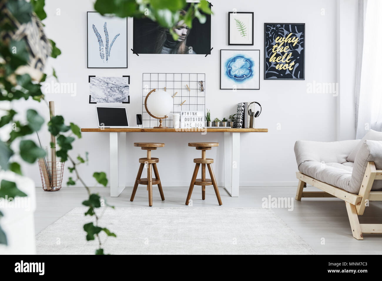 Acogedora habitación blanca con escritorio doble, carteles en la pared y sofá Foto de stock