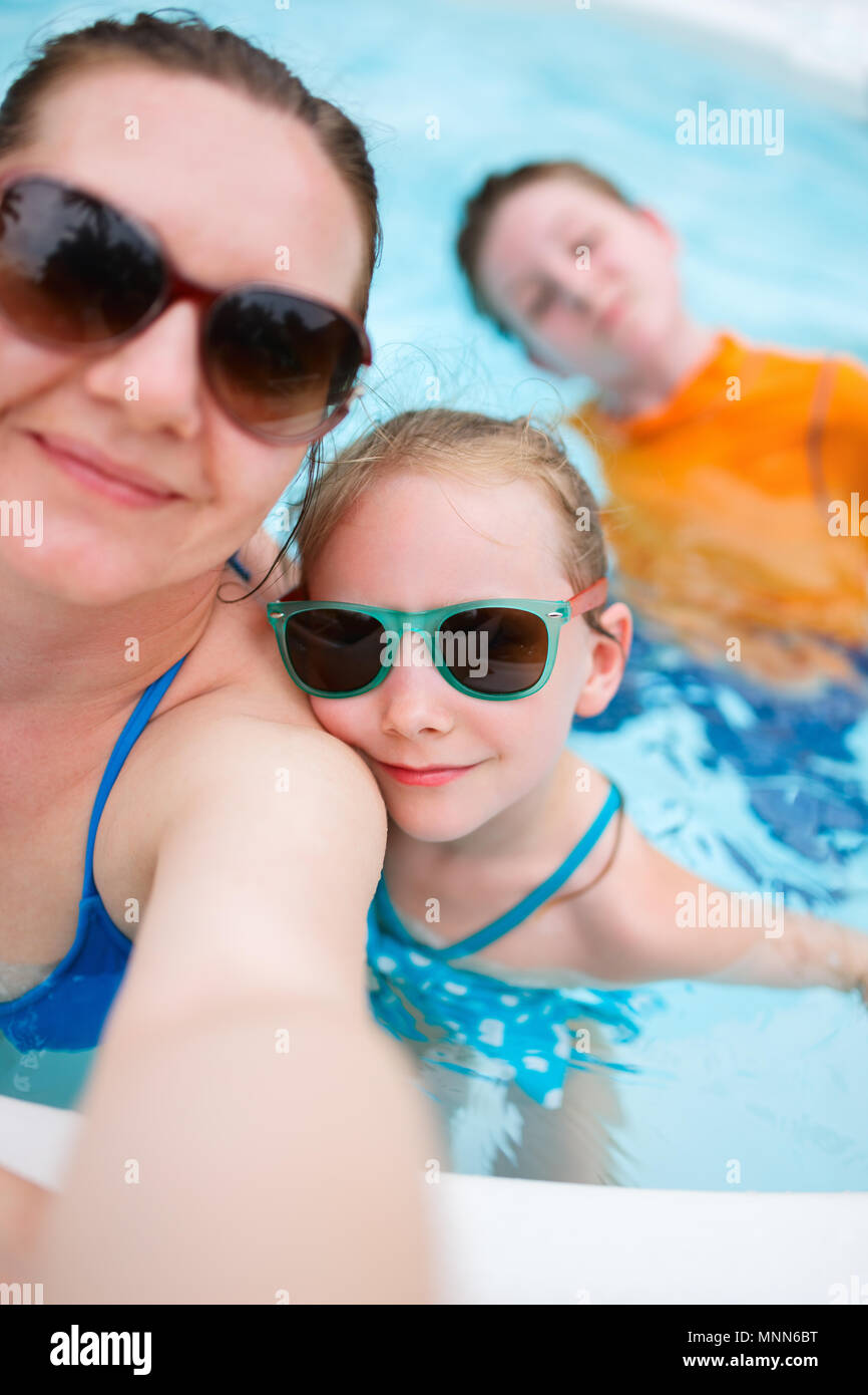 Feliz madre y sus hijos en una piscina al aire libre teniendo selfie en vacaciones tropicales Foto de stock