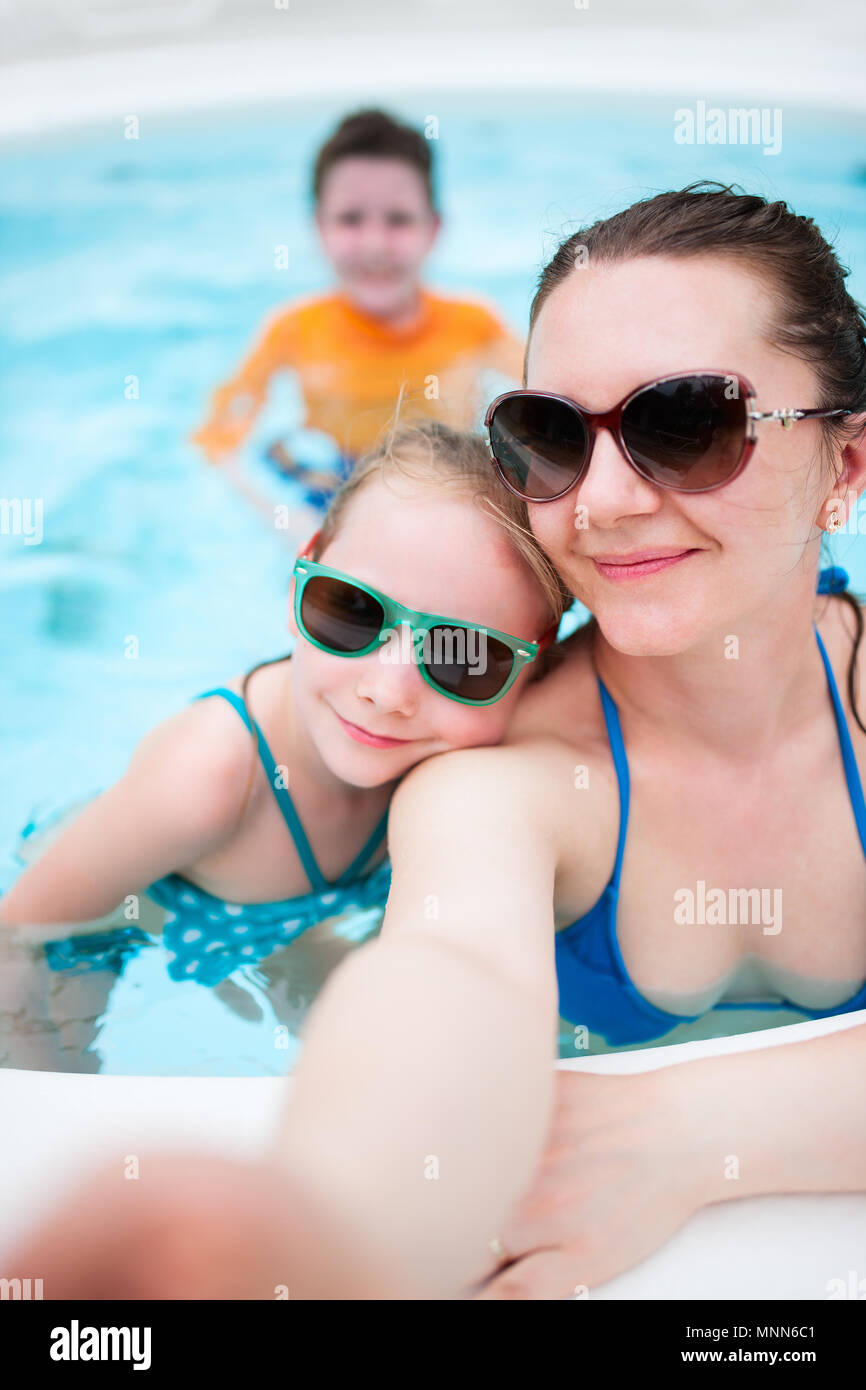 Feliz madre y sus hijos en una piscina al aire libre teniendo selfie en vacaciones tropicales Foto de stock
