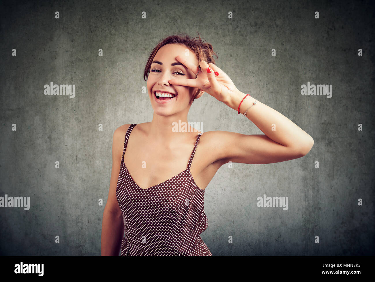 Retrato de una joven feliz que se encuentran aisladas sobre fondo de pared mostrando gestos de paz. Mirando a la cámara. Foto de stock