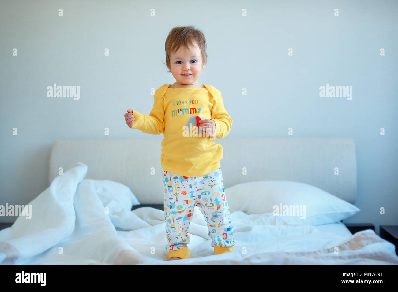 hijita de pie en la cama de sus padres. Bebé en pijama amarillo. Los niños duermen y ropa de cama desgaste Fotografía de stock - Alamy