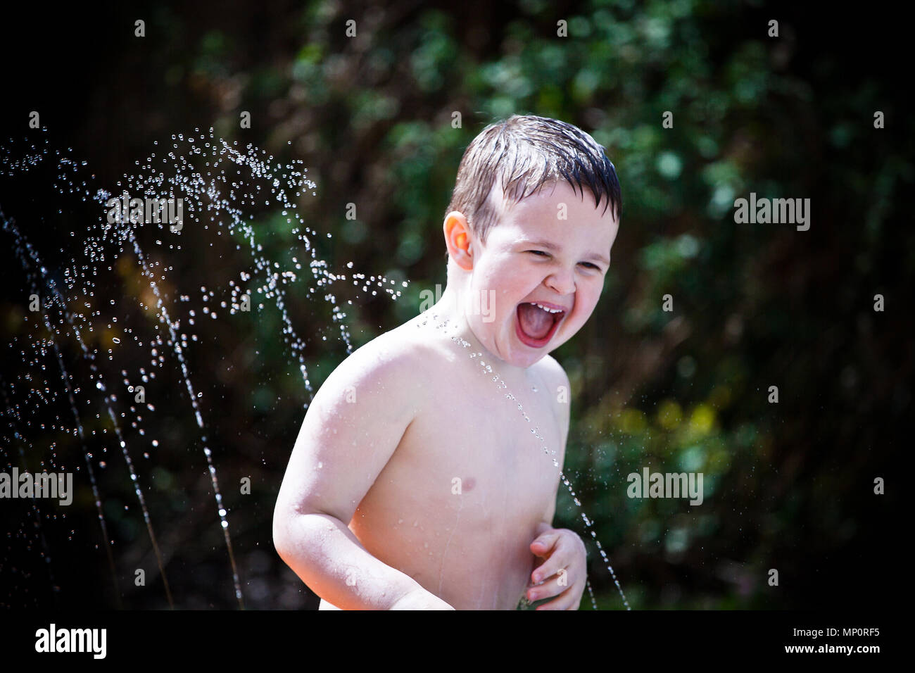 Joven jugando con rociadores de agua en el jardín de atrás Foto de stock