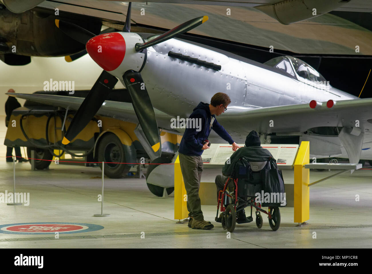Un hombre en una silla de ruedas mirando el Spitfire Mk 24 en el museo del aire de Duxford, Cambridgeshire, Inglaterra Foto de stock