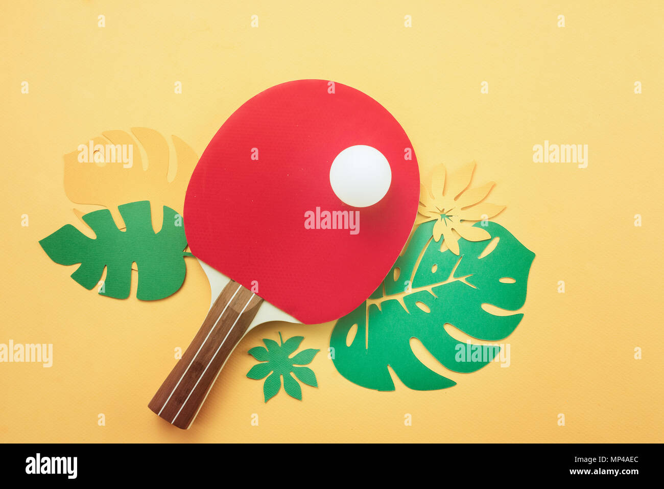 Ping pong raquetas y pelota con hojas tropicales. Deportes y recreación de verano piso yacía sobre un fondo amarillo soleado con espacio de copia. Foto de stock