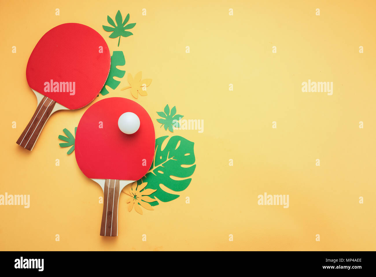 Ping pong raquetas y pelota con hojas tropicales. Deportes y recreación de verano piso yacía sobre un fondo amarillo soleado con espacio de copia. Foto de stock