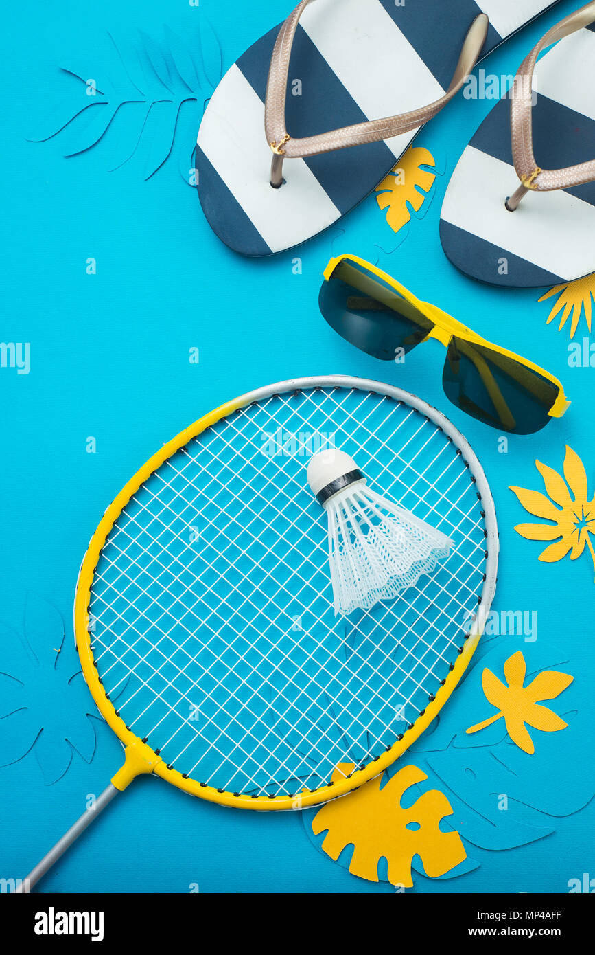 Playa de bádminton, flip flopsm gafas de sol y hojas tropicales. Deportes y recreación de verano piso yacía sobre un fondo azul brillante con espacio de copia. Foto de stock