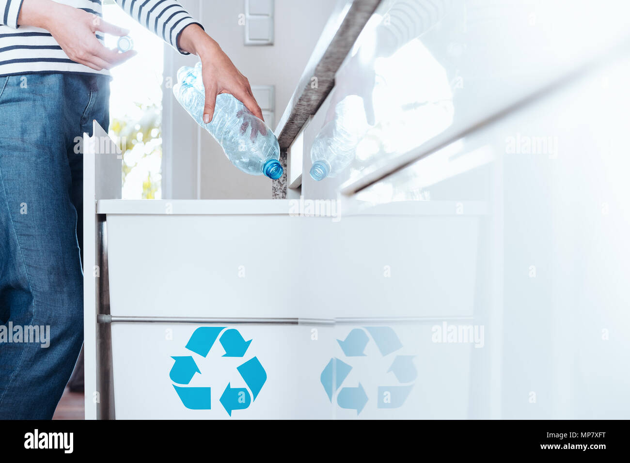 Persona con pro el comportamiento ambiental, poniendo la botella de plástico para cocina blanca bin con símbolo azul Foto de stock