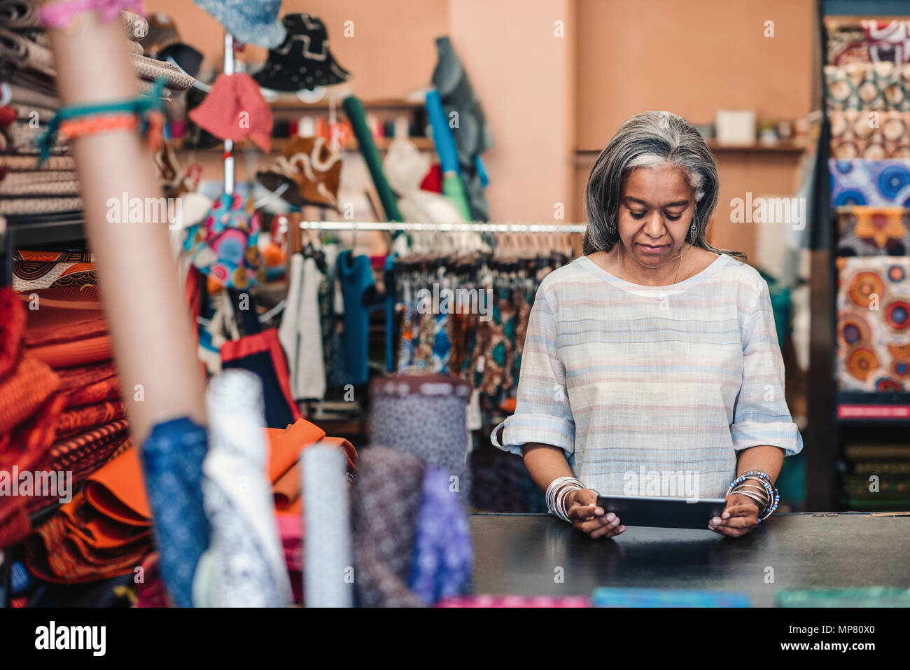 Mujer madura con una tableta digital en su tienda de tela Foto de stock