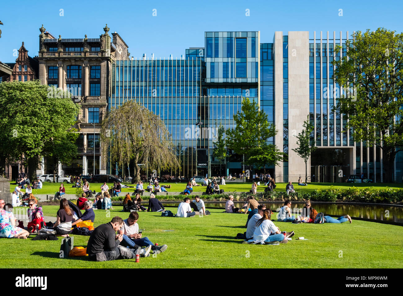 Gente sentada en la hierba de St Andrews Square en el cálido y soleado clima en Edimburgo, Escocia, Reino Unido, UK Foto de stock