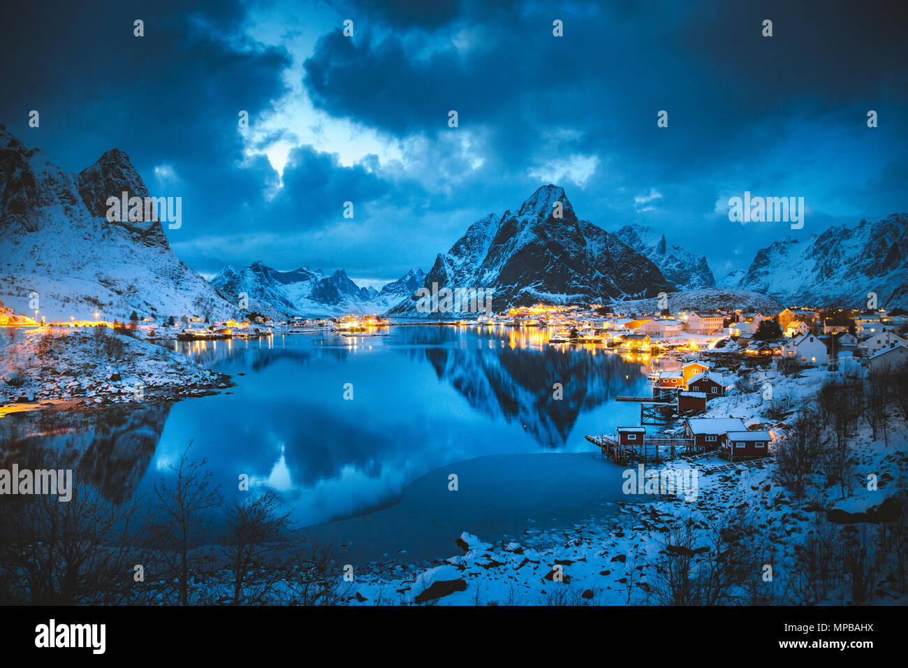 Vista clásica de la famosa aldea de pescadores de Reine con Olstinden pico en el fondo en la mágica noche de invierno crepúsculo, Islas Lofoten, Noruega Foto de stock