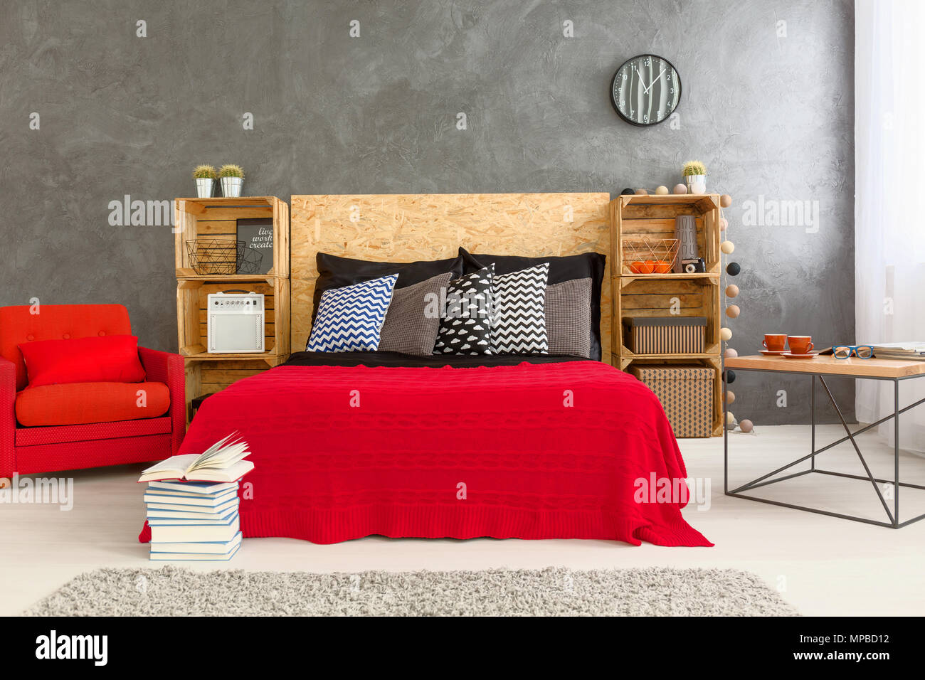 Habitación diseño moderno con cama sillón rojo sobre la pared gris de fondo. Estantes de madera hecha de de madera y cabecera de madera de la cama Fotografía de