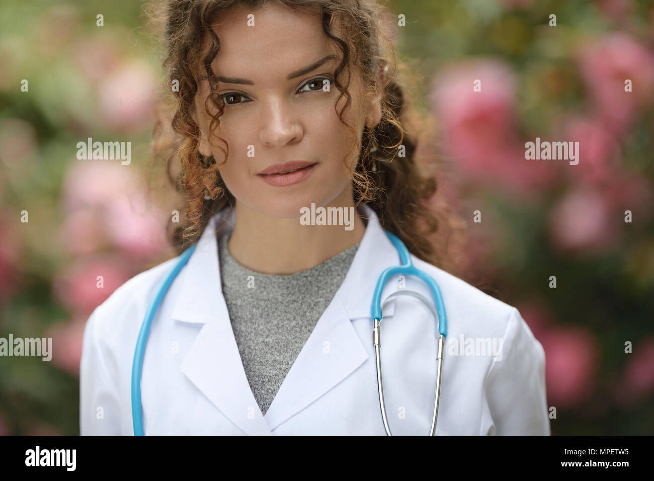 Retrato de una joven mujer, médico, profesional sanitario, médico, médico vistiendo una bata de laboratorio natural en entornos exteriores con blosso Foto de stock