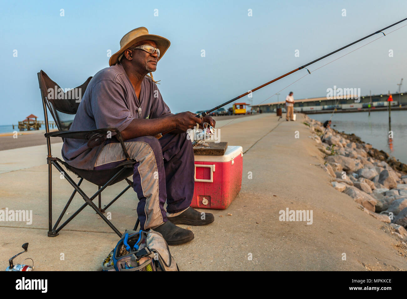 Hombre negro con gafas de sol pescando en el embarcadero del puerto deportivo municipal de Gulfport, en Gulfport, Mississippi Foto de stock