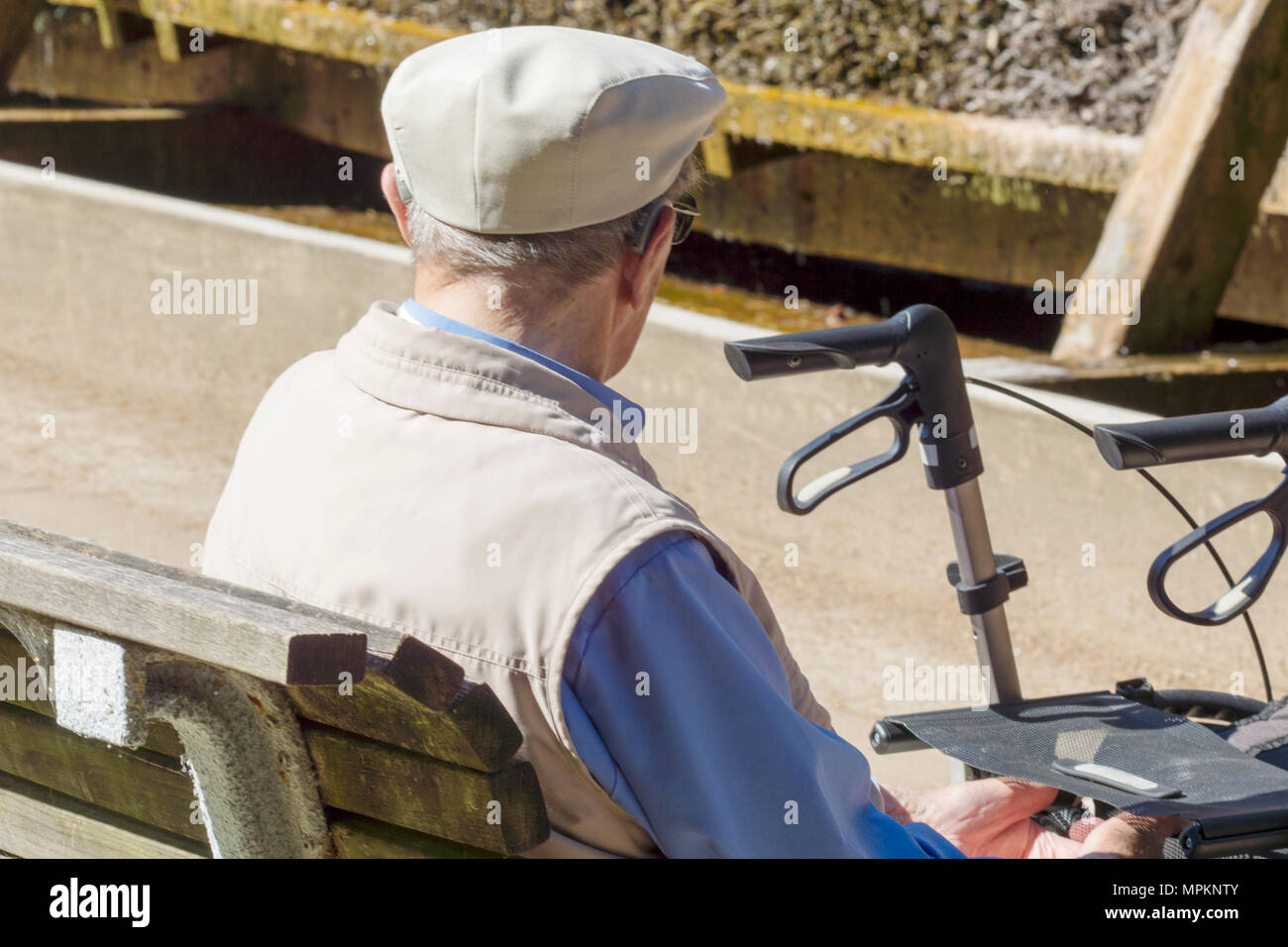 Un hombre viejo está sentado delante de su silla de ruedas en el parque y se está recuperando Foto de stock