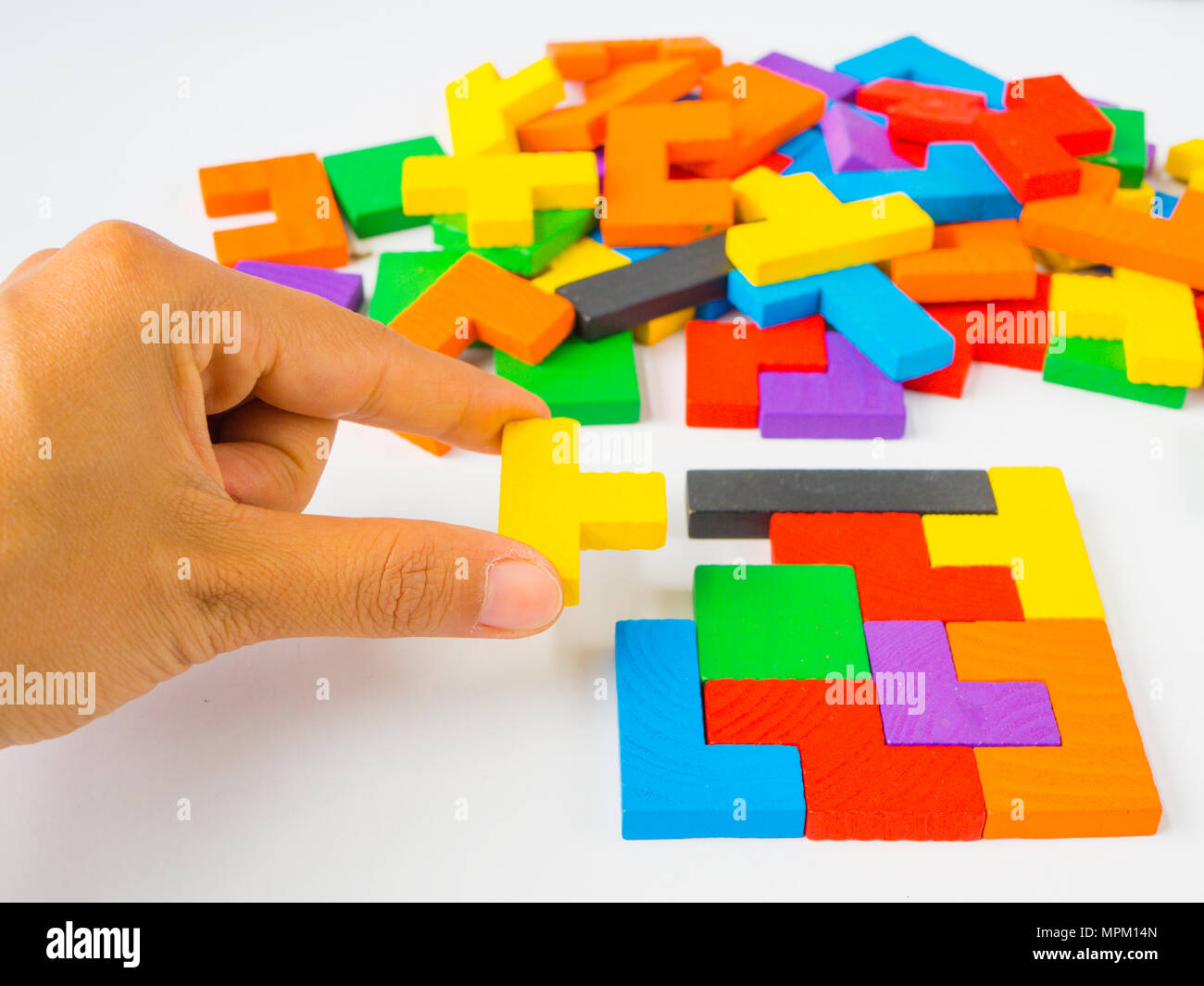 Mano sujetando la última pieza para completar un cuadrado tangram puzzle  coloridas de madera para kid sobre fondo blanco Fotografía de stock - Alamy