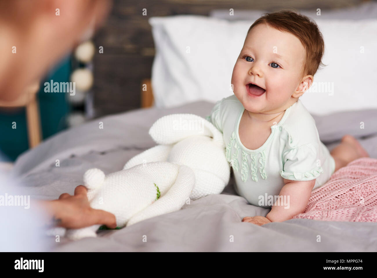 Bebé feliz con peluche en la cama en casa buscando a su madre Foto de stock
