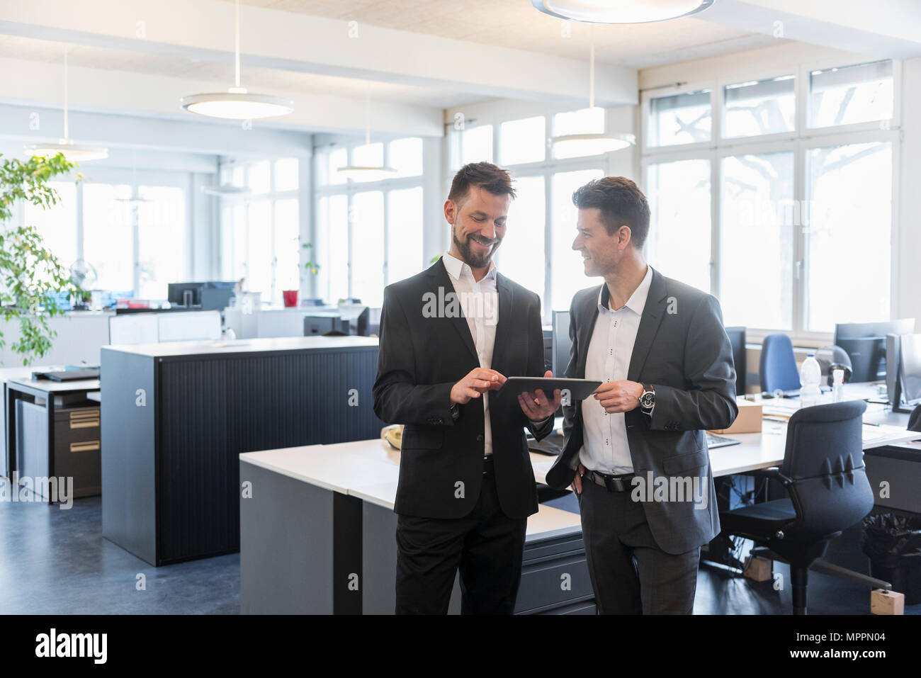 Dos hombres de negocios de pie en la oficina, discutiendo soluciones, utilizando tablet digital Foto de stock