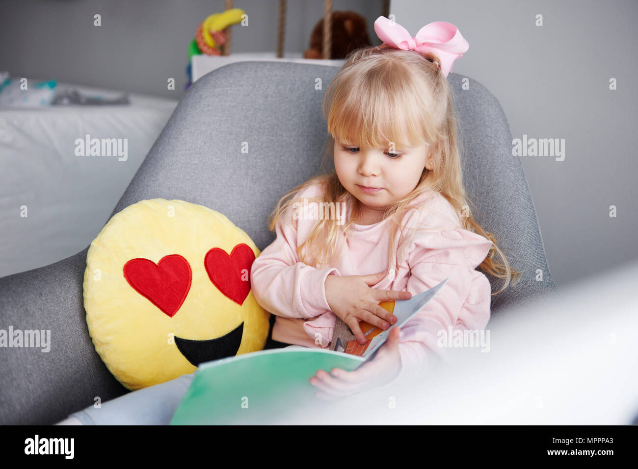 Retrato de niña rubia sentado en el sillón mirando al libro de imágenes Foto de stock