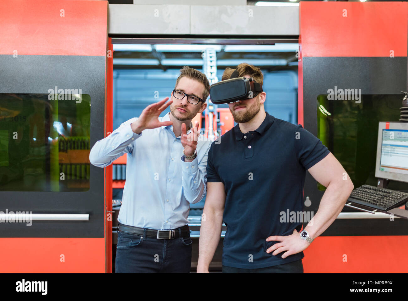 Hombre explicando la máquina a un colega llevaba gafas VR en la fábrica. Foto de stock