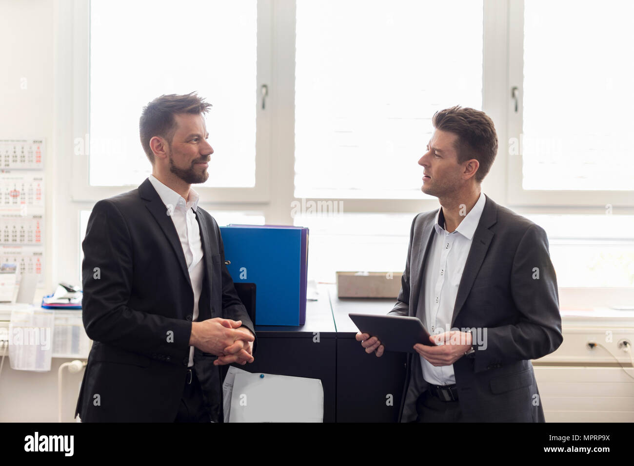 Dos hombres de negocios de pie en la oficina, discutiendo soluciones, utilizando tablet digital Foto de stock