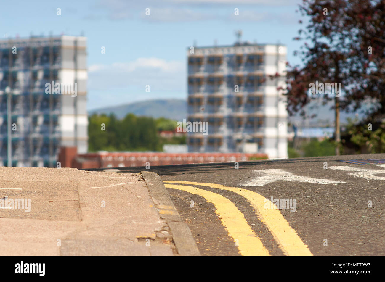 Marcas de línea doble amarilla en una calle local en Glasgow, Escocia, con una altura de edificios residenciales en el fondo. Foto de stock