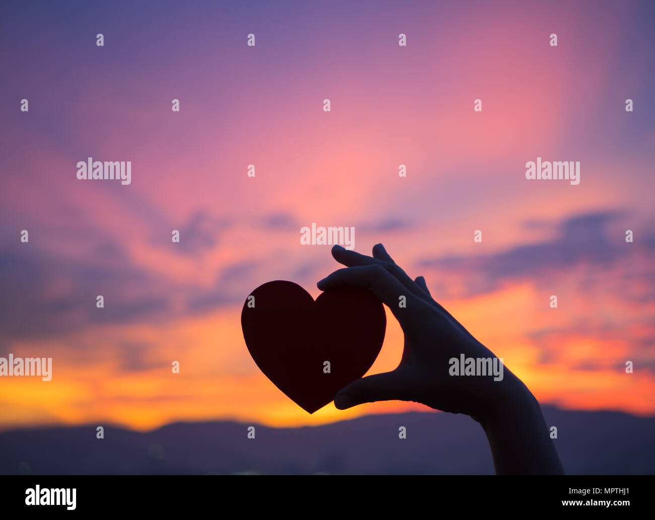 Silhouette mano sosteniendo hermoso corazón durante la puesta de sol de fondo. Feliz, el amor, el día de San Valentín idea, signo, símbolo, concepto. Foto de stock