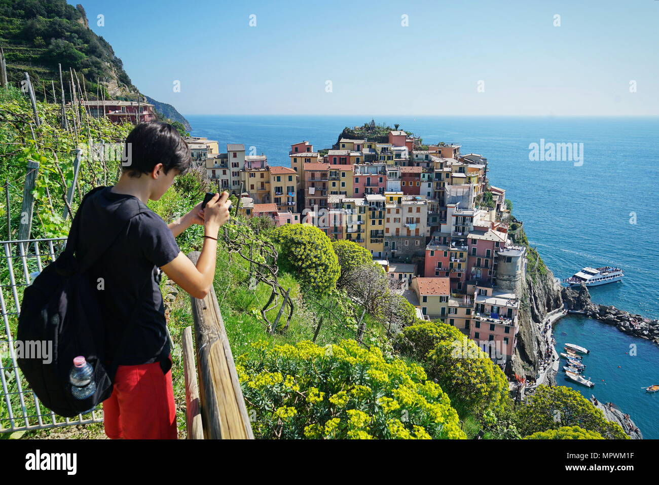 Un joven tomar una fotografía de la hermosa vista de Manarola ciudad. Es uno de los cinco famosos coloridos pueblos del Parque Nacional Cinque Terre en Italia Foto de stock