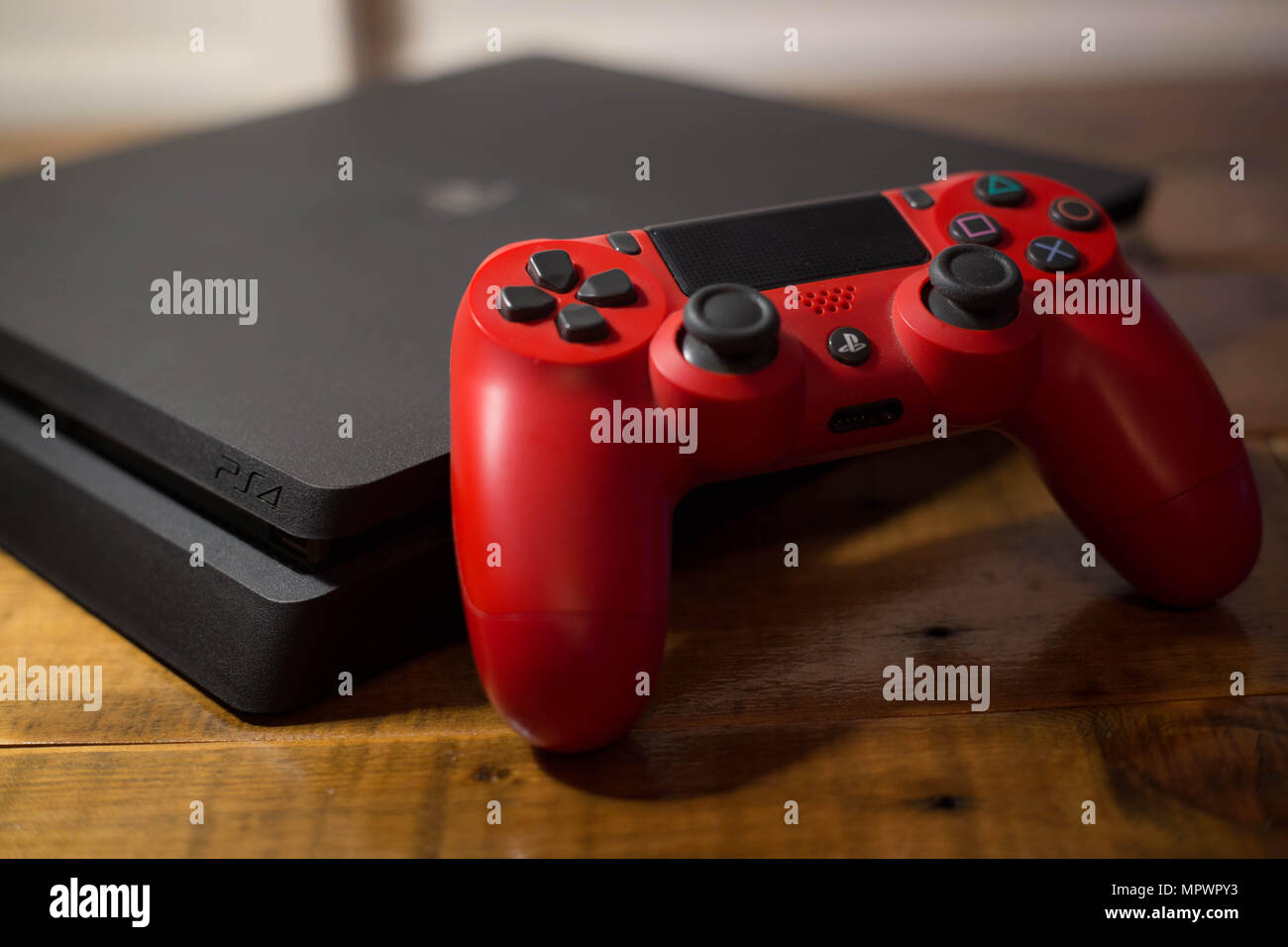 Una Sony PlayStation 4 consola de videojuegos con un controlador  inalámbrico rojo junto a ella. La PlayStation 4 o PS4 se conoce como inicio  de la octava generación de consola de video