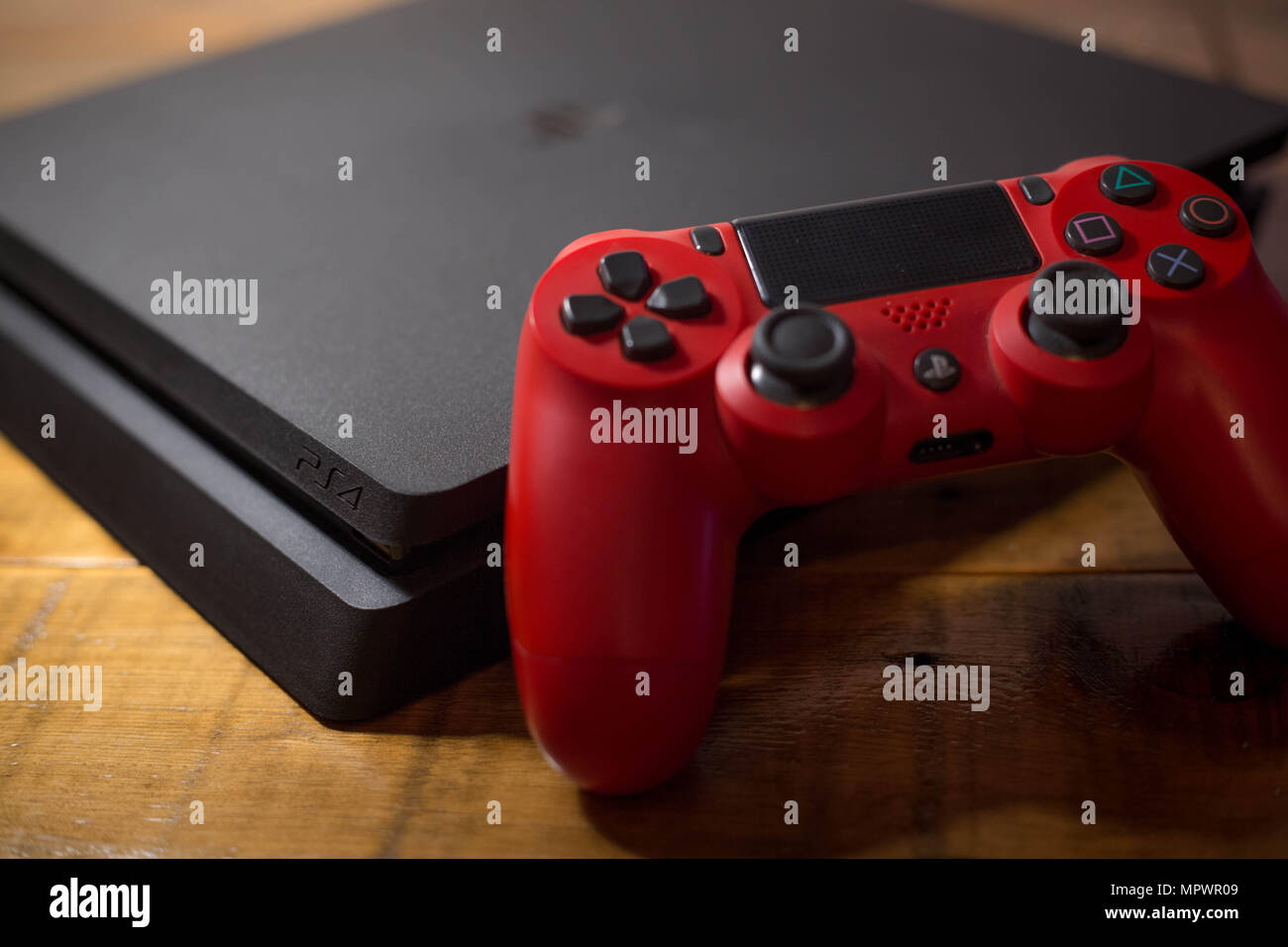 Una Sony PlayStation 4 consola de videojuegos con un controlador inalámbrico rojo junto a ella. La PlayStation 4 o PS4 se conoce como inicio de octava de consola de video