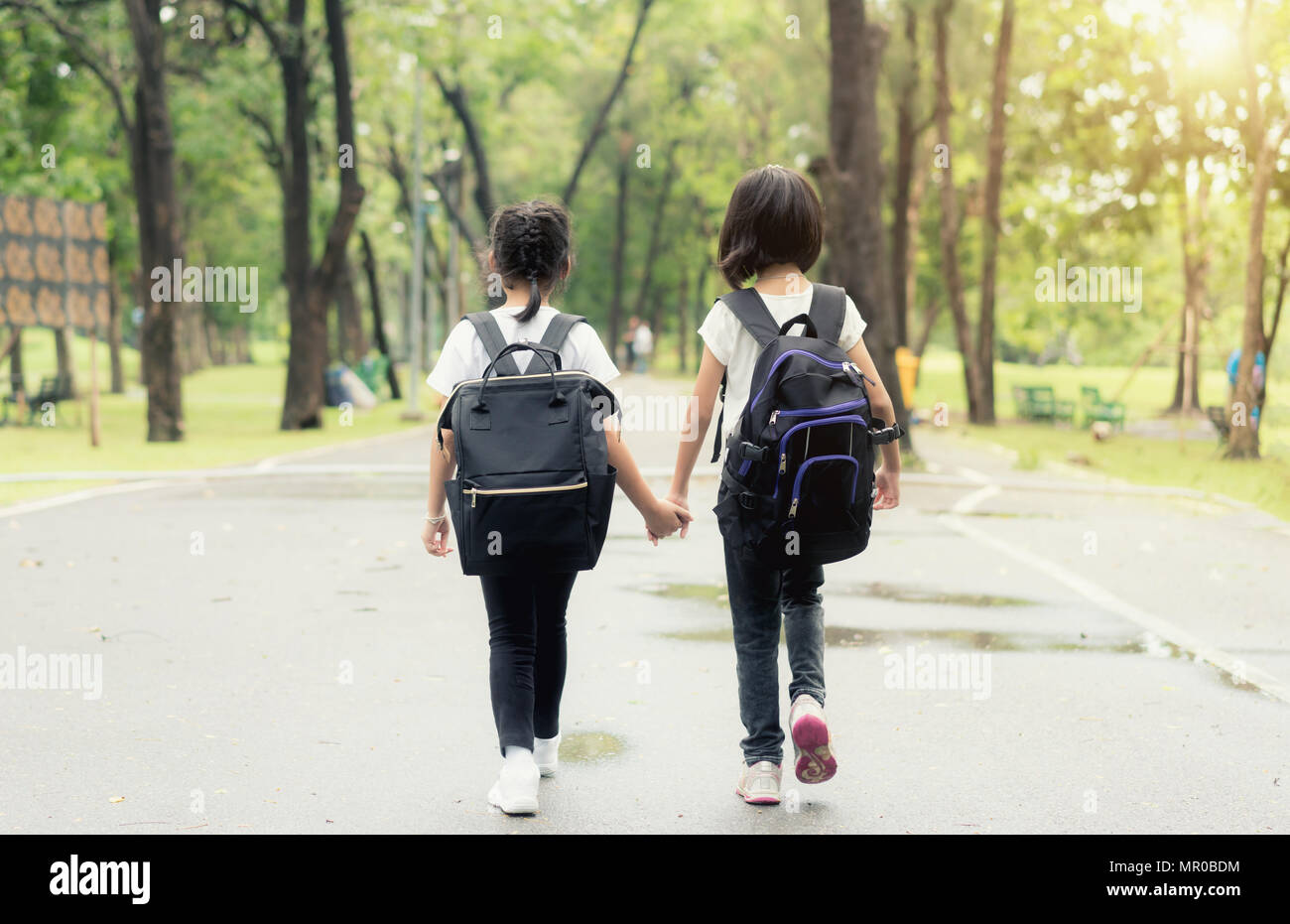 Dos alumnos de la escuela primaria van de la mano. Dos chica con mochilas  escolares detrás de la espalda. Cálido día de otoño. Al regresar a la  escuela. Poco de primer grado