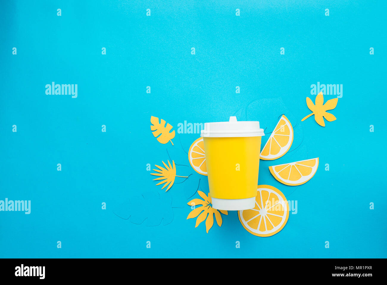 Vaso de papel con rodajas de limón y hojas tropicales sobre un fondo de color azul brillante. Copa de Verano para ir plana con copia espacio laical. Limonada desde arriba Foto de stock