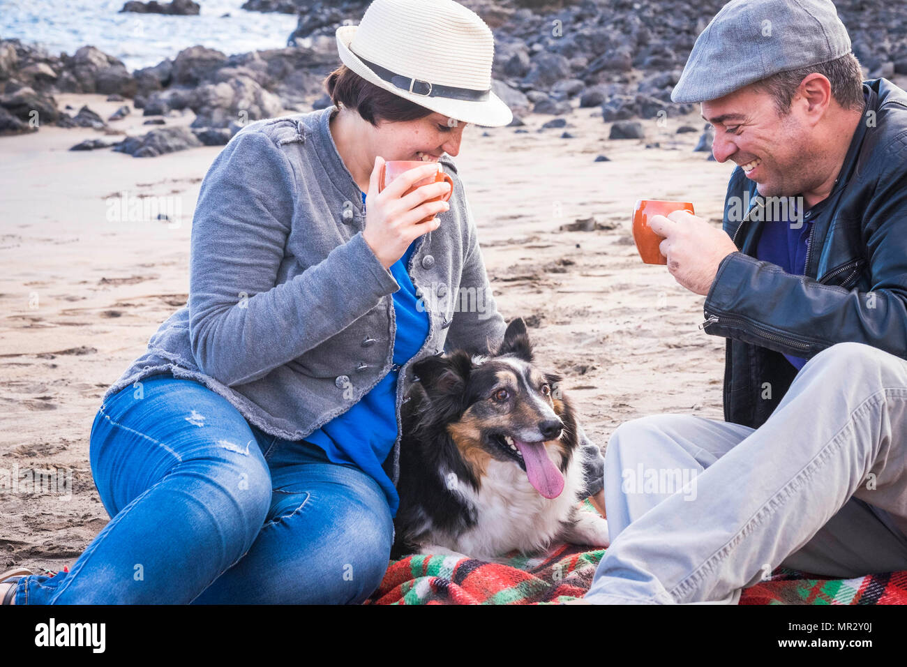 Hermosa pareja de mediana edad en el ocio en la playa de vacaciones en verano con una linda mascota Border Collie. Todos juntos con una taza de café a anejoy Foto de stock