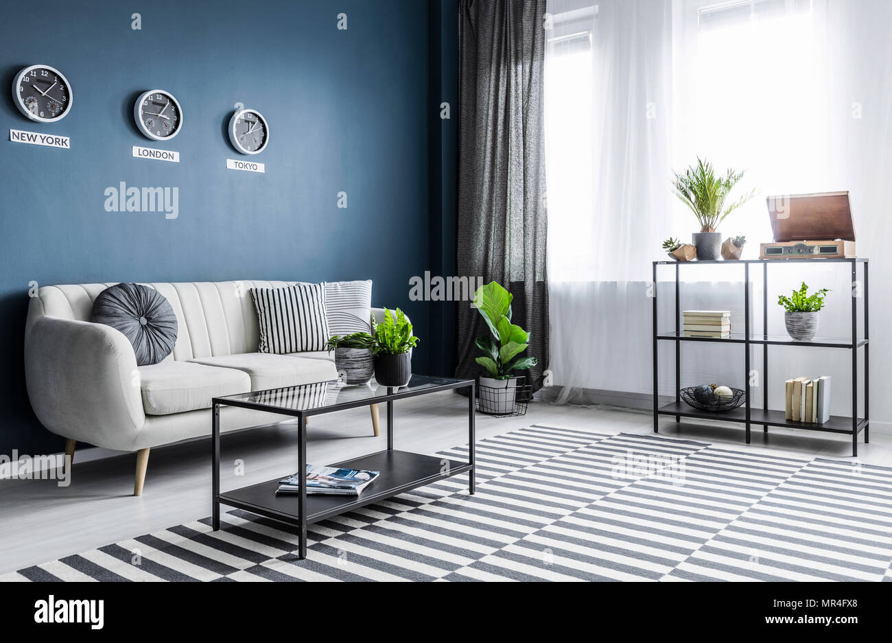 Plantas y alfombra de color azul brillante en el salón interior con relojes  arriba sofá beige Fotografía de stock - Alamy