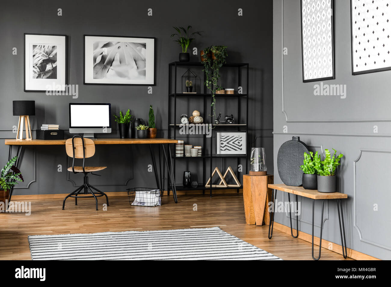 Rack negro con adornos de pie junto a una silla de madera y un escritorio  con lámpara, plantas y un ordenador en la oficina principal interior. Foto  real Fotografía de stock -