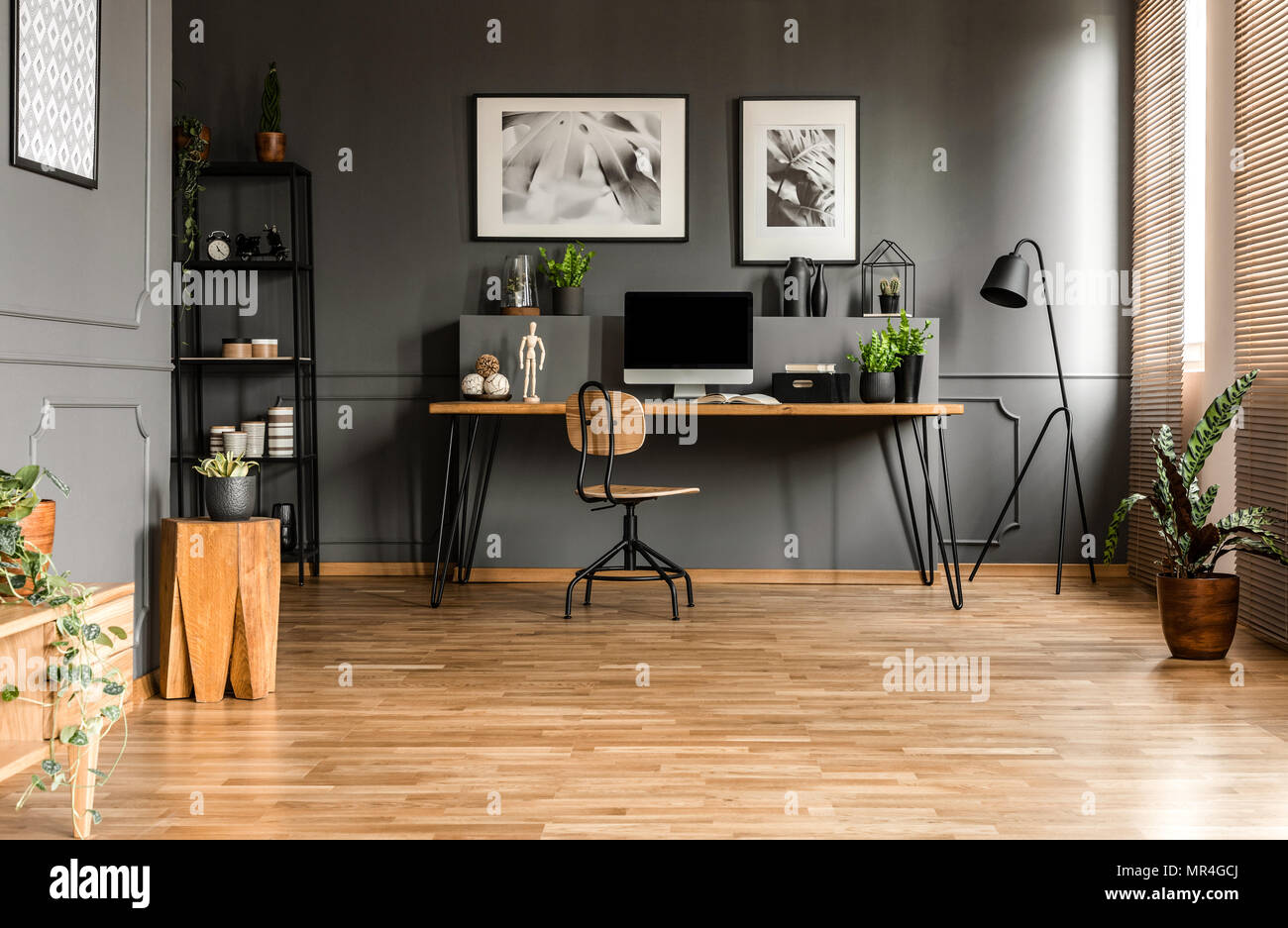 Foto real de la espaciosa oficina inicio interior con una sola silla en un  escritorio de madera con equipo y plantas de pie contra la pared con  moldura negra Fotografía de stock -